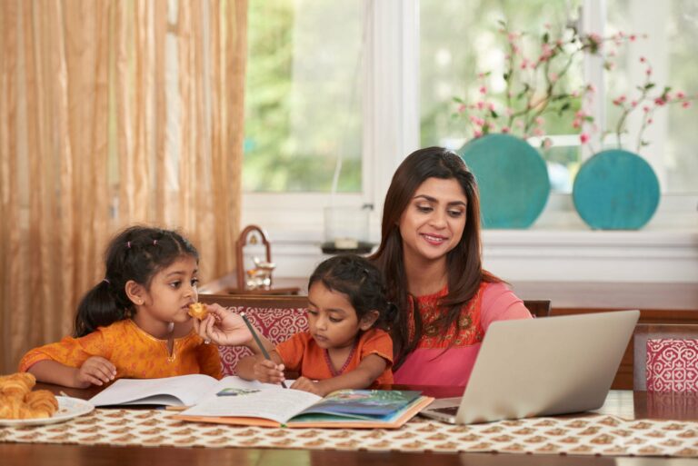 Cheerful pretty Indian woman working on laptop when babysitting