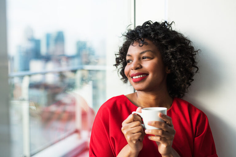 A close-up of a woman standing by the window holding coffee cup. Copy space.