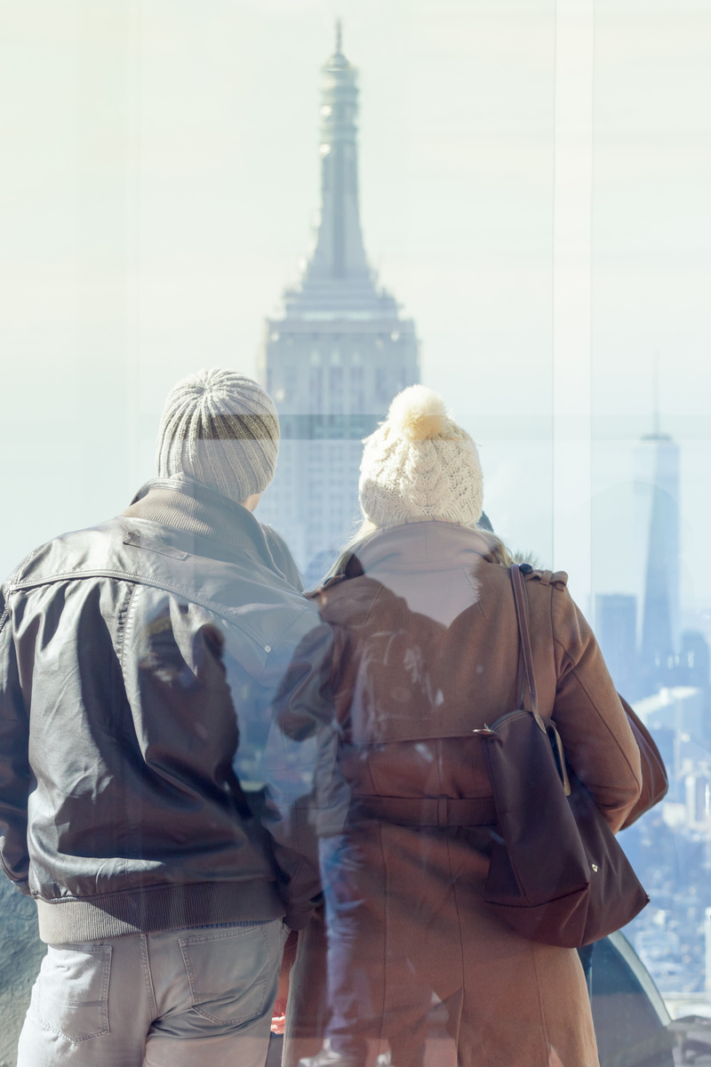 Romantic couple enjoying in New York City panoramic view. Manhattan downtown skyline with illuminated Empire State Building and skyscrapers seen from observation deck terrace.